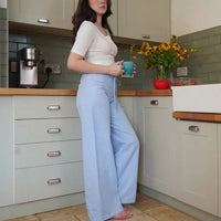 Woman wearing blue gingham short length pyjama bottoms with boxer fly in kitchen